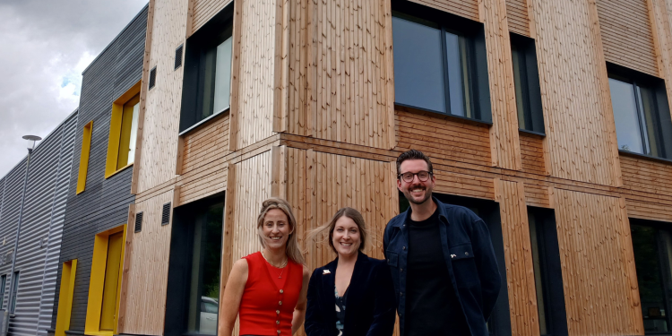 Three people stand smiling outside an industrial unit with a timber facade.