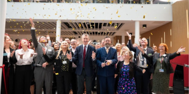 Golden confetti falls from the ceiling as a large group of well-dressed people cheer and wave their hands.