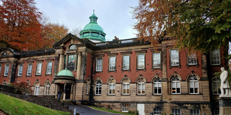 A grand, red brick hall with pillars at its entrance and a green tower above its roof