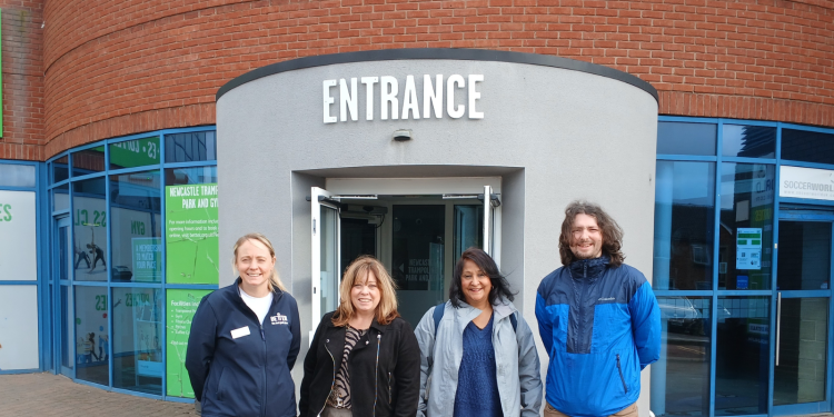 Four smiling people stand outside the entrance to Newcastle Trampoline Park, which is a red brick building with a grey revolving door entrance.