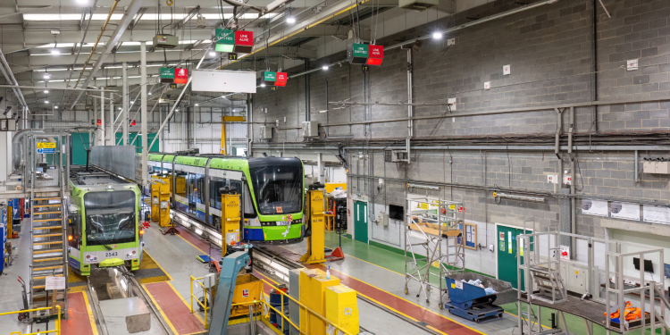 Inside a large, grey tram depot where two green and yellow trams are being worked on.