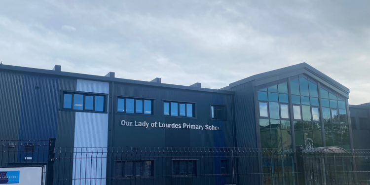 A grey and white school with a pointed roof to the right and lots of windows along the top