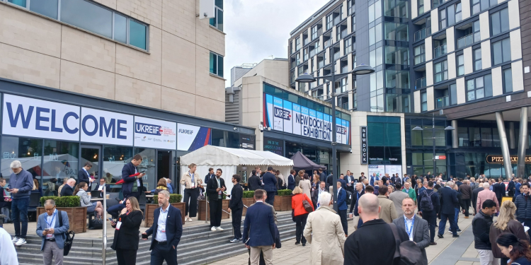 A busy conference with many people in front of an event hall and food stands.