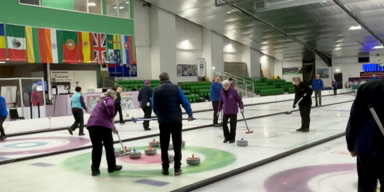 A group of curlers crowd around several stones on a target on the ice.