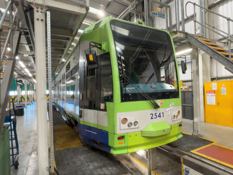 A green tram sits inside a depot with metal staircases on either side.
