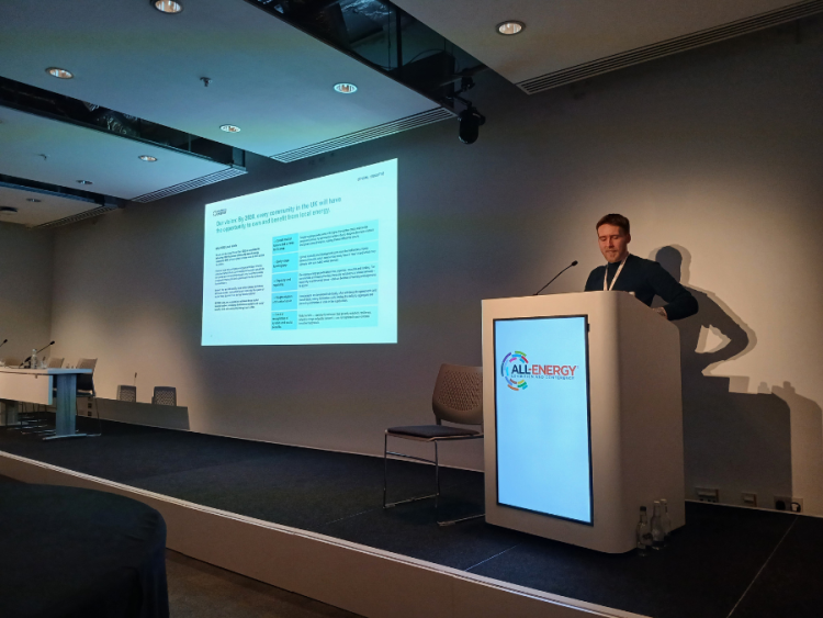 A man stands at a lecturn giving a powerpoint presentation
